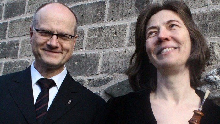 Ein Mann und eine Frau in Anzügen stehen vor einer Ziegelmauer.