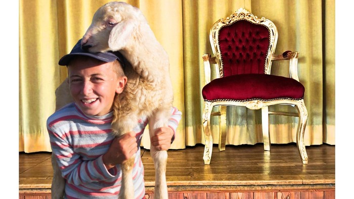 Junge hält Schaf, dahinter ein Königsthron