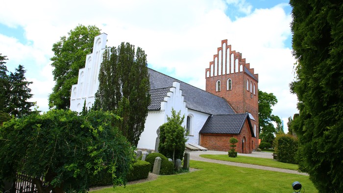 En hvid kirke med et rødt tårn og en smuk have.