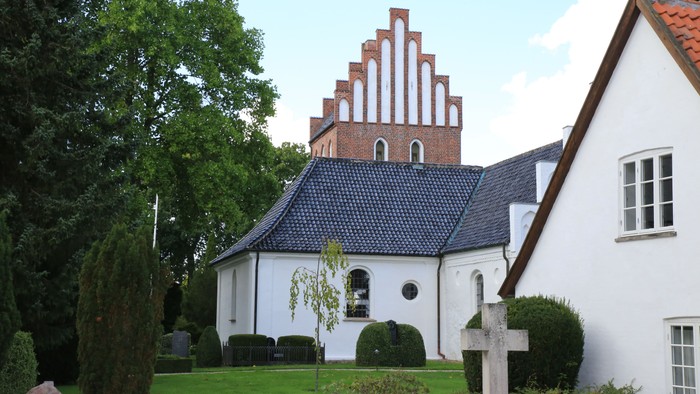 Hvid kirke med spiretårn og smukke træer