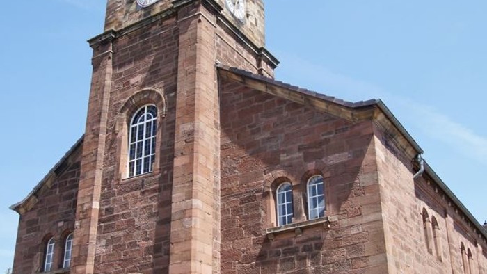 Alte Backsteinkirche mit hohem Glockenturm und Rundbogenfenstern.