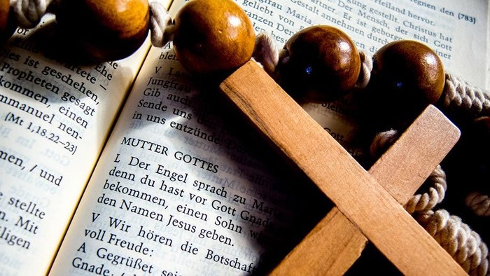Ein hölzernes Kreuz liegt auf einer deutschen Bibelseite mit Nüssen und einer Kerze