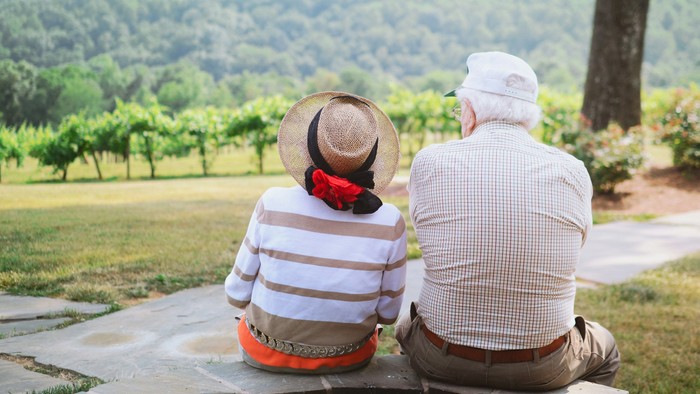 Ein älteres Paar sitzt auf einer Bank und blickt auf eine malerische Landschaft.