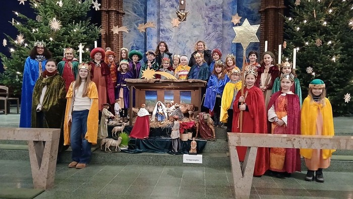 Eine Gruppe Kinder in farbenfrohen Gewändern posiert vor einer Weihnachtskrippe in einer Kirche