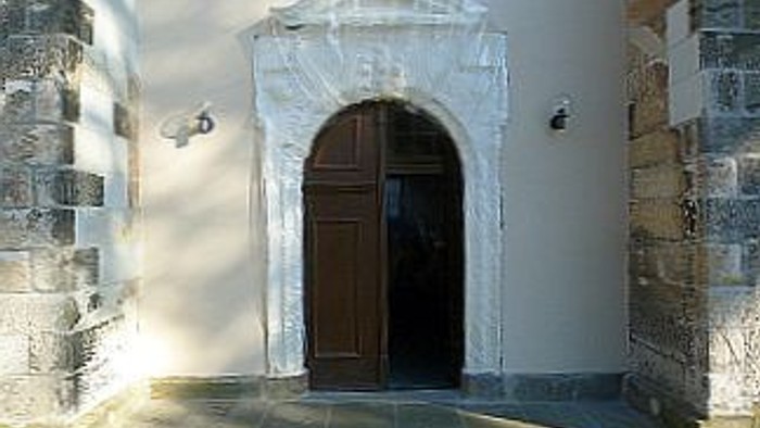 Das Bild zeigt einen alten Torbogen mit Holztür in einer Steinmauer.