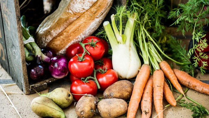 En samling af ferske grøntsager, heriblandt tomater, kartofler, rødbede og gulerødder, udstillet på en bjælke og en murstenet vegg