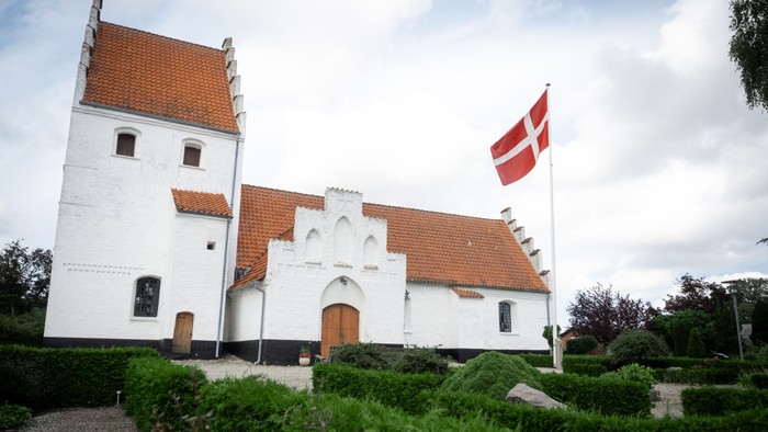 Hvid kirke med røde tag og dansk flag på tårn