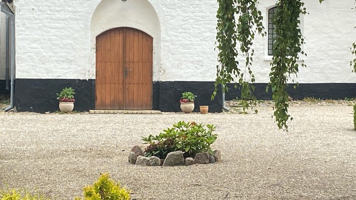 En hvid murstenet bygning med trædør og planter.