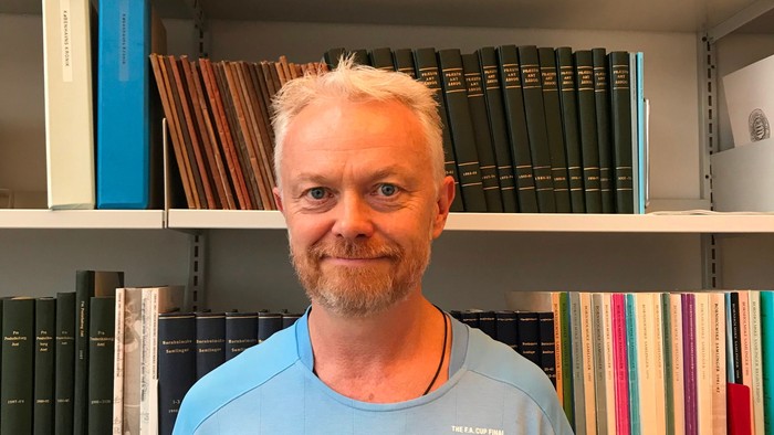 Mand står foran bookshelf med mange bøger.