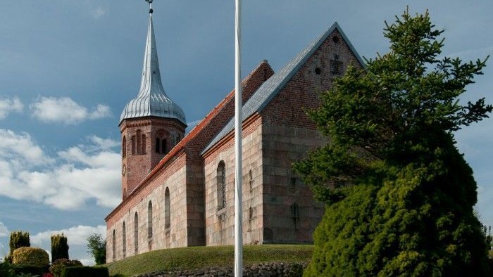 En kirke med spir med tårn og grønne buske foran
