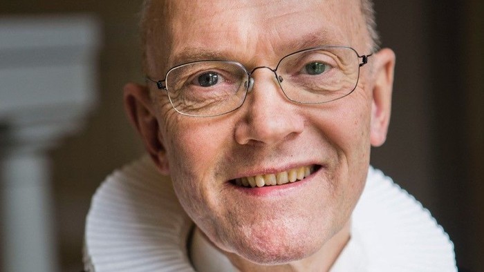 En smilende, eldre mand med glas og en hvid krage.