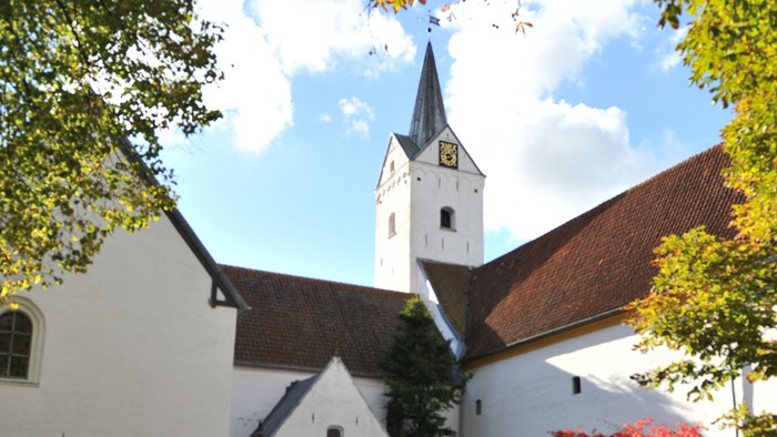 En hvid kirke med tårn og træer med faldne blade.