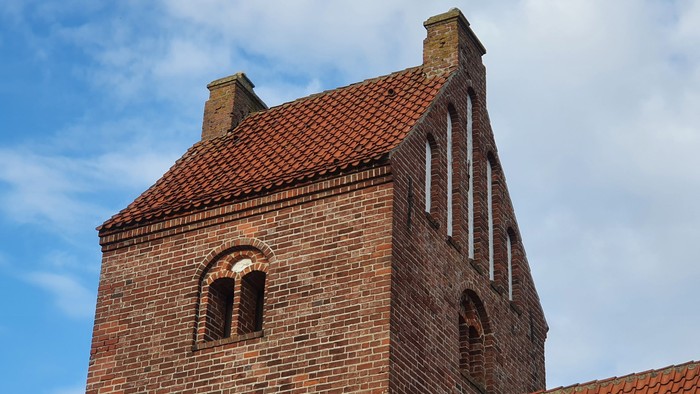 Røde teglkirke med to tårne og bjælkerøfter mod et blødt blå himmel.
