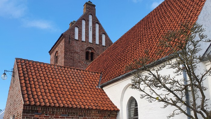 En lille kirke med røde tag og murstensvægge, med en benk foran.