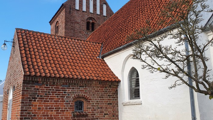 En lille kirke med røde tag og murstensvægge, med en benk foran.