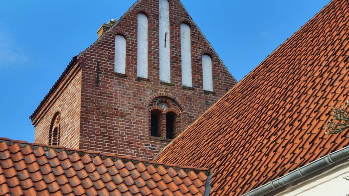 Røde teglstenskirke med tårn og små vinduer mod himlen