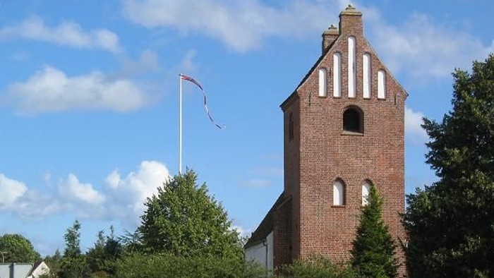 En rød murstenskirke med tårn og hvide vinduer ved en vej.