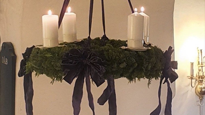 En hængende kranse med grønne blade og sorte bænder med tre lysstaker.