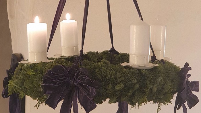 En hængende kranse med grønne blader og fire lyse lygter, smykket med sorte bælter