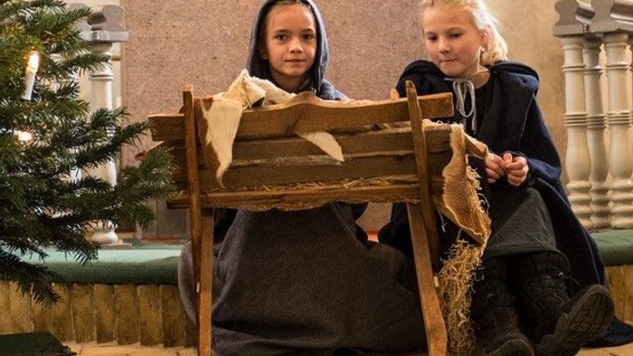 To børn sidder på en træstol med skinn og klæder.