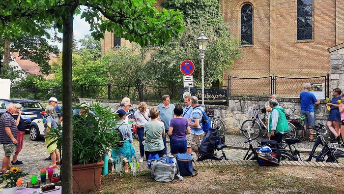 Eine Gruppe von Menschen steht vor einem Backsteingebäude, einige mit Fahrrädern, und unterhalten sich.