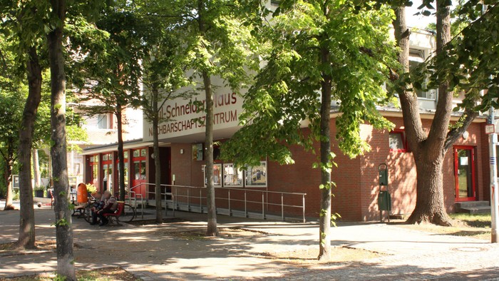 Ein rotes Gebäude mit Schildern, umgeben von Bäumen und einem Gehweg.