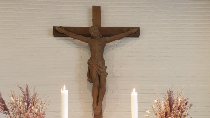 En altertavle med kors, lysestage og blomsterarrangementer