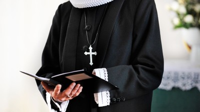 En præst holder en bog og bærer en halskæde med et kors.