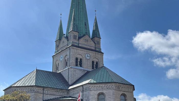 En stor kirke med to spirer og en klokke, med flag i forgrunden