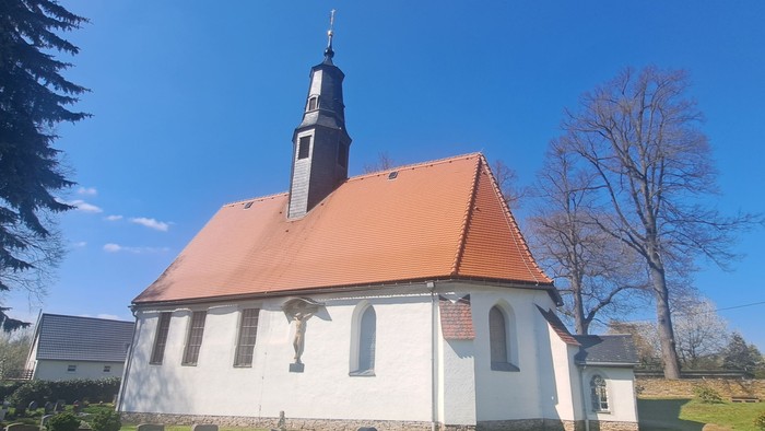 Kleine weiße Kirche mit rotem Dach und hohem Turm unter blauem Himmel