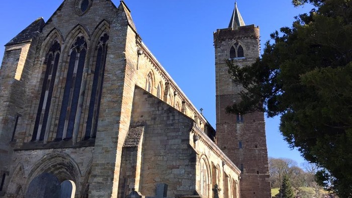 Old stone church with tall tower and arched windows, surrounded by gravestones.