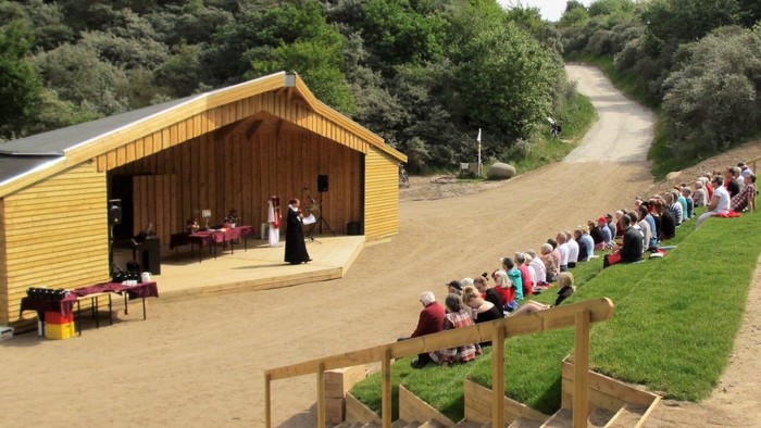En gruppe af mennesker ser en teaterforestilling på en scenekonstruktion i skoven