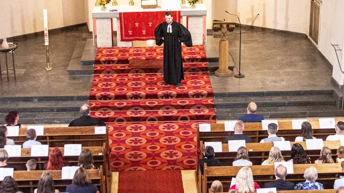 Ein Priester steht vor einem Altar in einer Kirche, umgeben von Gläubigen.