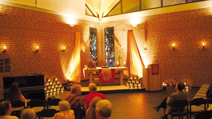 Gottesdienst in einer Kirche, Menschen sitzen auf Stühlen, Priester am Altar