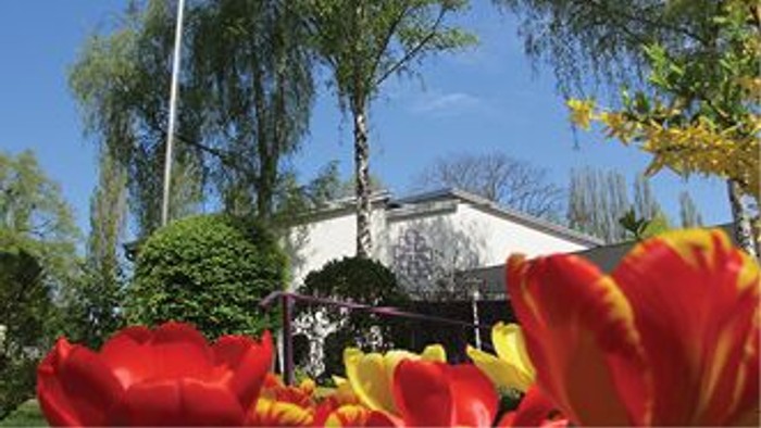 Ein weißes Haus mit rotem Dach, umgeben von Bäumen und leuchtenden Blumen im Vordergrund