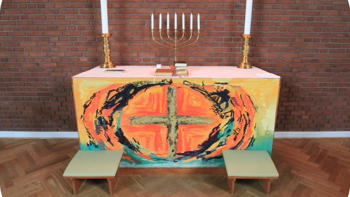 Altaret i kirken med farverig dækkede bord og to benker foran