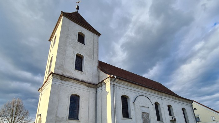 Alte Kirche mit hohem Turm auf grasigem Hügel unter bewölktem Himmel