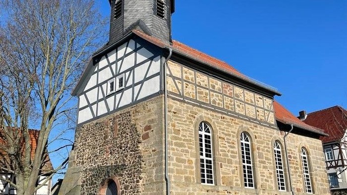 Kleine Steinkirche mit hölzernem Oberbau und hohem Turm, vor einem klaren blauen Himmel.