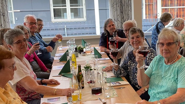 En gruppe pensionister sidder ved lange bord og spiser.