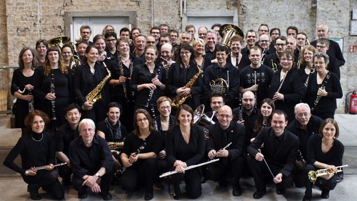 Ein großer Musikensemble posiert mit Instrumenten in einem Raum