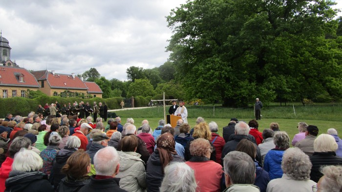 Große Menschenmenge versammelt sich im Freien, ein Mann spricht vor einem Kreuz
