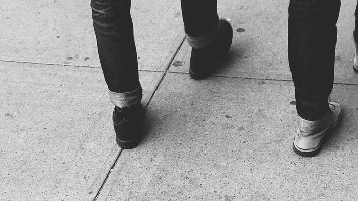 Three pairs of feet walking on a sidewalk.
