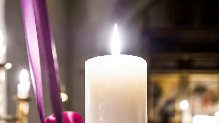 En lysende lyse med lilla bånd og gran.