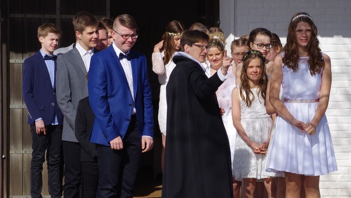 En gruppe ungdomme og unge står i en kreds, nogle i formelt tøj, mens en person i sort klæder står i midten.