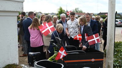 En gruppe danskere holder flag og omgiver en mørk vogn.