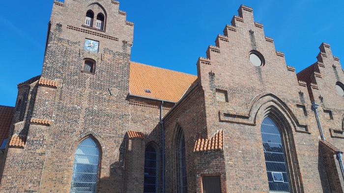 Gamle teglsteinskirke med spisse tårn og buevinduer under klar blå himmel