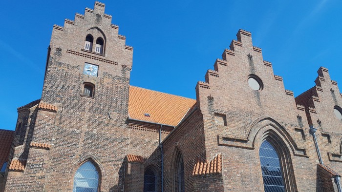 Gamle teglsteinskirke med spisse tårn og buevinduer under klar blå himmel
