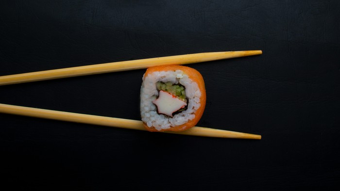 Ein Sushi-Rollenstück wird mit Stäbchen gehalten