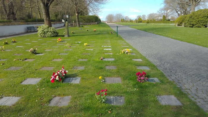 En park med grønne græsplæner og små gravsteder med blomster.