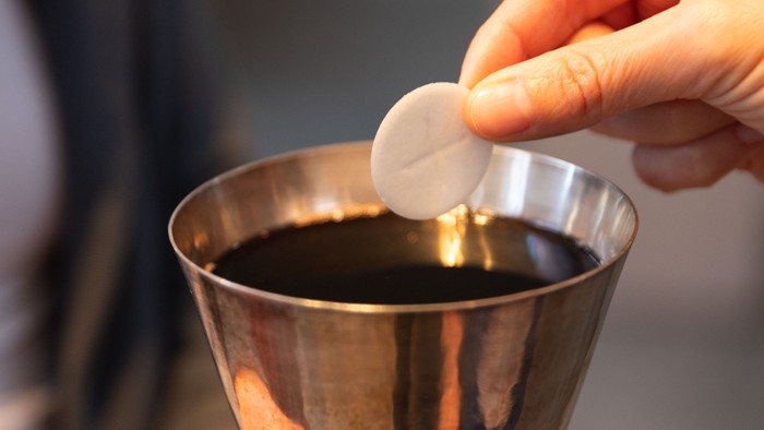 Hand legt eine Hostie in einen Kelch.